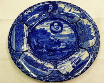Puede incluir: Plato de cerámica azul y blanco con un diseño decorativo que representa escenas de la historia de la ciudad de Nueva York. El centro del plato representa el desembarco de Hendrick Hudson, con el texto "Landing of Hendrick Hudson, 1609".