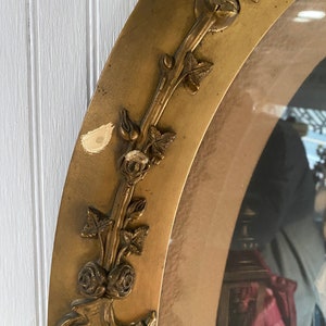 May include: A gold oval picture frame with a decorative floral design. The frame has a worn, antique look and is slightly chipped in places.