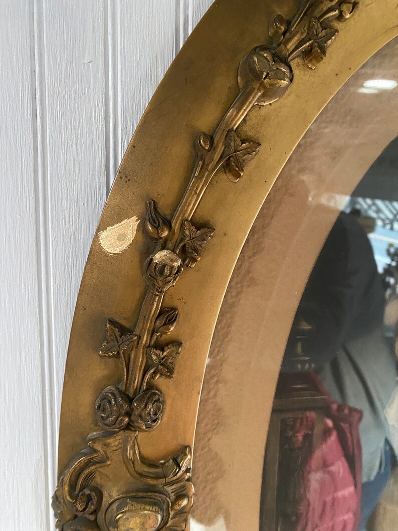 May include: A gold oval picture frame with a decorative floral design. The frame has a worn, antique look and is slightly chipped in places.