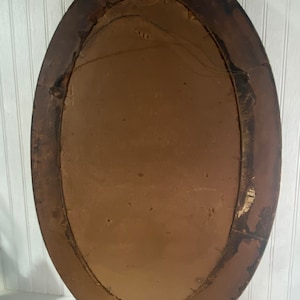 May include: An oval-shaped wooden picture frame with a brown finish. The frame has a simple design and is in good condition.