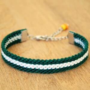 Könnte beinhalten: Ein geflochtenes Armband in Grün und Weiß mit einem silbernen Verschluss und einer kleinen orangefarbenen Perle.