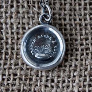 Peut inclure: Un collier en argent avec un pendentif en forme de sceau de cire qui dit "Tenez Garde a Vous".