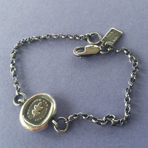 Peut inclure: Un bracelet en argent avec un charme représentant une feuille de chêne et le texte "The Grace of Growth". Le bracelet a un fermoir en argent et un design en chaîne.