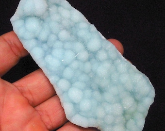 Op de afbeelding: Een lichtblauw, onregelmatig gevormd, plat stuk mineraal met een bubbelig, getextureerd oppervlak. Het mineraal heeft een witte, ondoorzichtige kern en een doorschijnende, lichtblauwe buitenlaag.