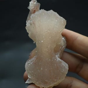 以下が含まれることがあります： 半透明で淡いピンクがかった白色の鉱物標本で、扇のような結晶構造をしています。このクラスターは、ギザギザとした質感の縁と、中心に向かって細くなる繊細な層状の形成が特徴で、自然な光の屈折を見せています。