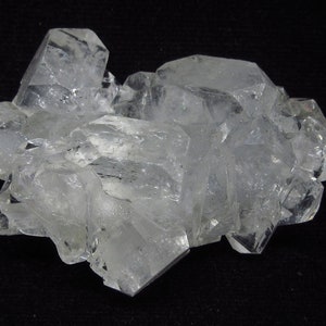 Puede incluir: Un grupo de cristales de cuarzo transparentes con una variedad de formas y tamaños. Los cristales son translúcidos y tienen un brillo vítreo.
