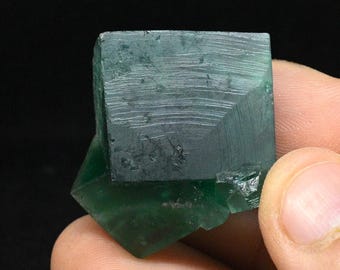 Könnte beinhalten: Ein leuchtend grüner Fluoritkristall mit kubischer Form und Streifen auf seiner Oberfläche.