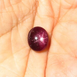 May include: A deep red star ruby gemstone with a star-like reflection in the center.
