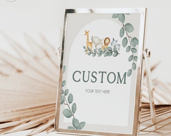 May include: A printable sign with a light grey background and a green leafy border. The sign features a watercolour illustration of a giraffe, elephant, lion, and zebra. The text "CUSTOM" is printed in dark green, and the text "YOUR TEXT HERE" is printed in black.