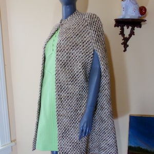 May include: A brown and white tweed cape with a collar and long sleeves. The cape is on a mannequin and has a slight A-line shape.