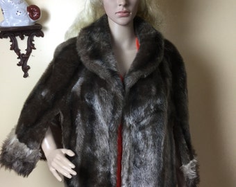 May include: A brown faux fur jacket with a wide collar and three-quarter sleeves. The jacket is worn over a red top and a plaid skirt. A mannequin displays the vintage outerwear.