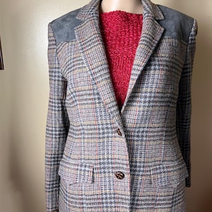 May include: A gray plaid blazer with brown and red accents. The blazer has suede shoulder patches and two front pockets.