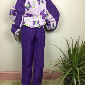May include: A vintage purple tracksuit. The jacket features a butterfly print on a light purple background, with solid purple sleeves and collar. The matching pants are a solid purple color. The tracksuit is displayed on a mannequin.