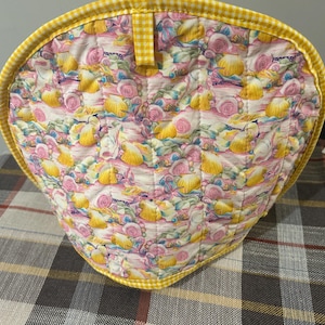 May include: Yellow and pink floral patterned teapot cozy with a yellow gingham trim.