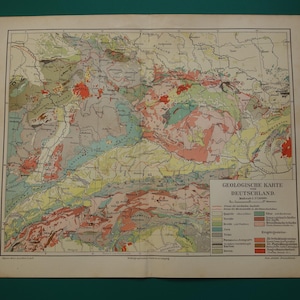Może przedstawiać: Zabytkowa mapa geologiczna Niemiec, przedstawiająca szczegółowo formacje geologiczne kraju. Mapa wykorzystuje różne kolory do reprezentowania różnych rodzajów skał i cech geologicznych. Widoczny jest tytuł "GEOLOGISCHE KARTE DEUTSCHLAND".