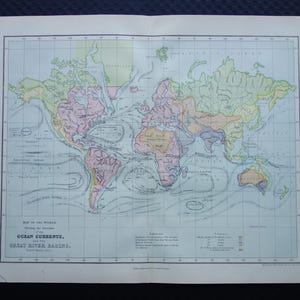 Puede incluir: Antiguo mapa del mundo que muestra las corrientes oceánicas y las grandes cuencas fluviales. El mapa presenta continentes en tonos rosa, verde y amarillo, con océanos azules y corrientes etiquetadas. El título está impreso en negro, con texto adicional y una cuadrícula.