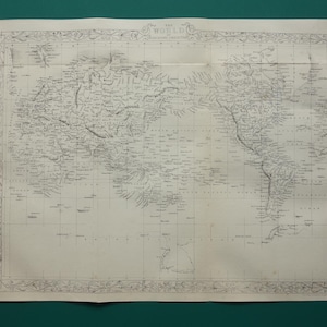 Op de afbeelding: Een vintage zwart-wit wereldkaart gedrukt op gebroken wit papier, voorzien van een decoratieve rand met gedetailleerd lijnwerk. De kaart toont geografische labels en rasterlijnen, met de titel "THE WORLD" gecentreerd aan de bovenrand.