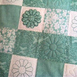 May include: A green and white quilt with a floral pattern. The quilt is made of squares with different designs, including a large flower in the center of each square.
