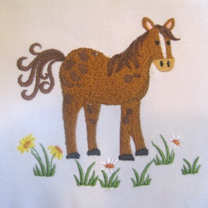 May include: Embroidered brown horse with a white stripe on its face standing in a field of green grass and white daisies.