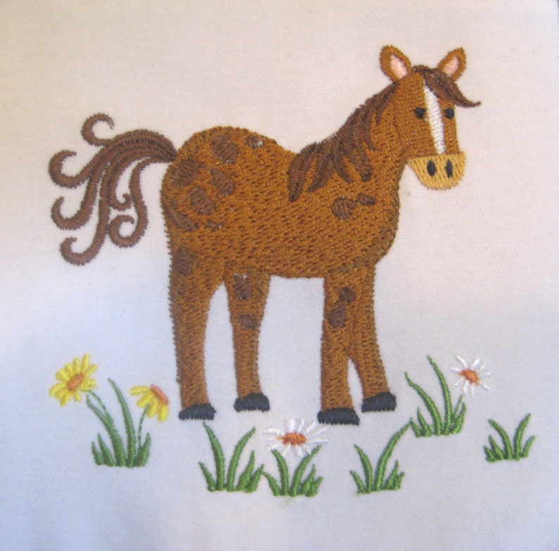 May include: Embroidered brown horse with a white stripe on its face standing in a field of green grass and white daisies.