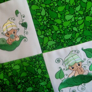 May include: A white fabric baby quilt with a green peapod design. Each square features a cute embroidered baby in a peapod. The background fabric is a green paisley pattern.