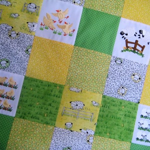 May include: A patchwork quilt with a yellow, green, and white color scheme. The quilt features a repeating pattern of chicks and sheep.