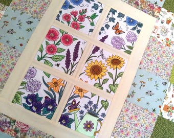 Puede incluir: Un edredón floral con un diseño de ventana, que presenta seis cuadrados con diferentes ilustraciones de flores e insectos. Las flores incluyen flores rosas, moradas y amarillas, con un colibrí, una mariposa y una abeja. El edredón tiene un borde color crema.