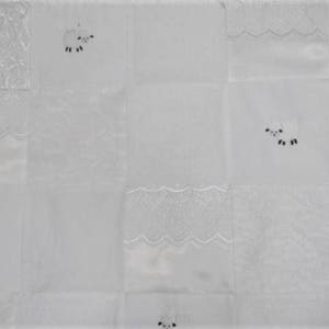 K&ouml;nnte beinhalten: Wei&szlig;e Steppdecke mit Patchwork-Design mit gestickten Schafen und Spitzenbesatz.