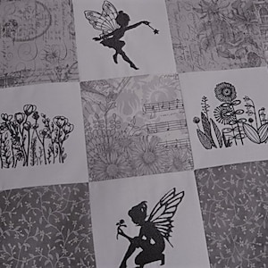 May include: A gray and white patchwork quilt with black embroidered images of fairies, flowers, and musical notes.