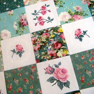 May include: A patchwork quilt with a floral design. The quilt is made of squares of different fabrics, each with a different floral pattern. Some of the squares have embroidered roses in the center.