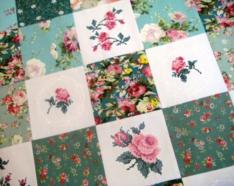 Puede incluir: Una colcha de retazos con un diseño floral. La colcha está hecha de cuadrados de diferentes telas, cada uno con un patrón floral diferente. Algunos de los cuadrados tienen rosas bordadas en el centro.