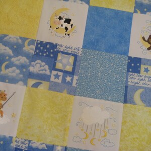 May include: A patchwork quilt with a blue and yellow color scheme. The quilt features embroidered images of a cow, a bear, a giraffe, and clouds with stars and moons. The text "star light, star bright" is embroidered on the quilt.