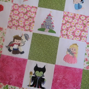 May include: A patchwork quilt with a variety of embroidered images, including a castle, a princess, a prince, a rose, a spinning wheel, and a fairy tale character. The quilt is made of white fabric with pink and green floral patterns.