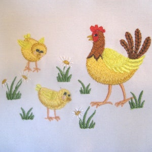 May include: Embroidered design of a yellow hen with a red comb and two yellow chicks. The hen is standing on a white background with green grass and white flowers.