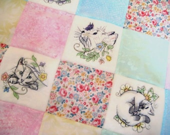 Puede incluir: Una colcha de retazos con un patrón floral e imágenes bordadas de gatos. La colcha está hecha de varios tonos de tela rosa, azul y blanca.
