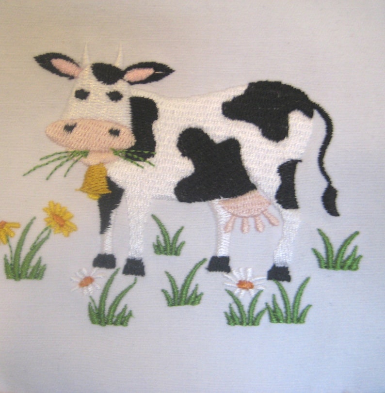 May include: Embroidered design of a black and white cow with a pink nose, eating green grass. The cow is standing in a field of green grass with yellow flowers and white daisies.