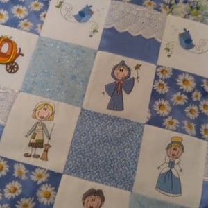 May include: A blue and white patchwork quilt with embroidered images of a carriage, a fairy godmother, Cinderella, and birds. The quilt is made of different fabrics, including satin, lace, and cotton.