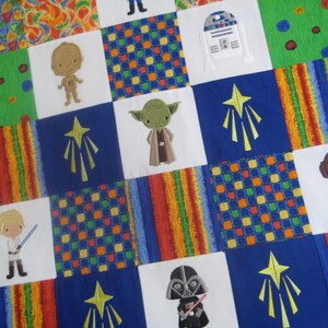 Puede incluir: Una colcha de retazos colorida con personajes de Star Wars bordados, incluyendo Yoda, Darth Vader, la princesa Leia, R2-D2 y Luke Skywalker. La colcha tiene un esquema de color azul, verde, rojo, amarillo y blanco.