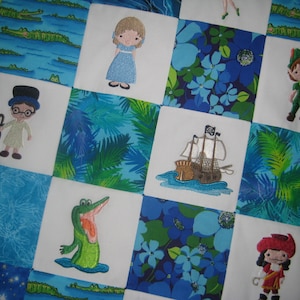 May include: A patchwork quilt featuring embroidered images of characters and scenes from Peter Pan. The quilt includes images of Peter Pan, Wendy, Captain Hook, a crocodile, and a pirate ship, set against a backdrop of blue and green floral and aquatic patterns.