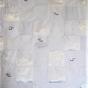 K&ouml;nnte beinhalten: Wei&szlig;e Patchwork-Decke mit gestickten Schafen und einem Zitat aus der Bibel: "Er sammelt die L&auml;mmer in seine Arme und tr&auml;gt sie nahe an seinem Herzen." Lukas 15,20.