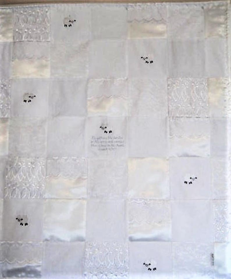 K&ouml;nnte beinhalten: Wei&szlig;e Patchwork-Decke mit gestickten Schafen und einem Zitat aus der Bibel: "Er sammelt die L&auml;mmer in seine Arme und tr&auml;gt sie nahe an seinem Herzen." Lukas 15,20.