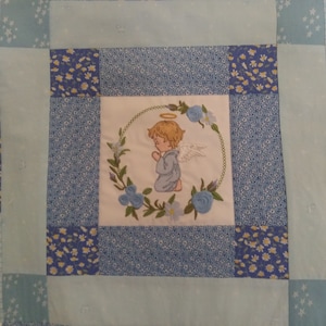 May include: A blue and white patchwork quilt with an embroidered image of a praying angel in the center.