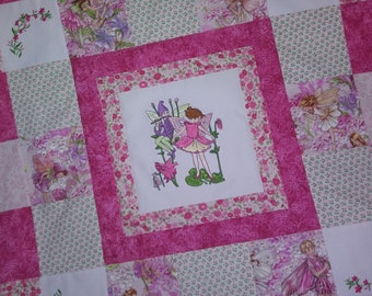 Puede incluir: Una colcha de retazos rosa y blanca con un cuadrado central que presenta una imagen bordada de dos hadas. Las hadas están rodeadas de flores y hojas.