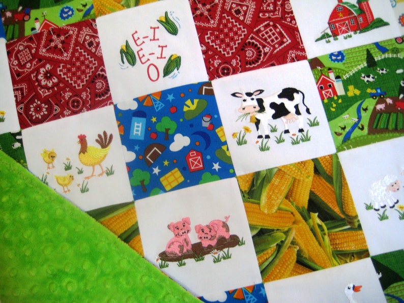 May include: A white and green patchwork quilt with various embroidered images, including a cow, a pig, a chicken, corn, and a red barn. The quilt is made of different fabrics and textures, and the embroidery is detailed and colorful.