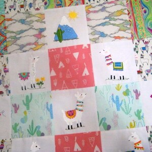 May include: A patchwork quilt featuring various square blocks with colorful designs. The quilt showcases embroidered llamas, cacti, mountains, and clouds. The color palette includes pink, blue, green, and white, creating a cheerful and whimsical aesthetic.