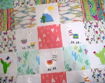 Puede incluir: Un edredón de retazos con bloques cuadrados que muestran diseños bordados. El edredón presenta llamas, cactus, montañas y nubes. La paleta de colores incluye rosa, azul, verde y blanco, creando una estética alegre y caprichosa.