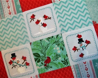 Puede incluir: Un edredón de retazos con muñecos de nieve bordados y cardenales rojos. El edredón combina telas rojas, blancas y turquesas con diseños de chevron y florales. Los muñecos de nieve llevan sombreros y bufandas.