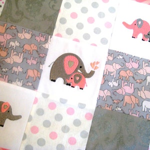 May include: A pink and gray baby quilt with a patchwork design featuring embroidered elephants with hearts. The quilt is made of soft fabric and is perfect for a nursery.