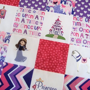 May include: A white fabric quilt with a patchwork design featuring a princess, a castle, a horse, and the phrase "Once Upon A Time" repeated in different colors and fonts.