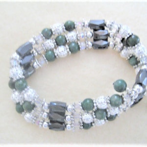 May include: A multi-strand bracelet with green, silver, and black beads. The bracelet is made of various materials, including glass, metal, and gemstones.